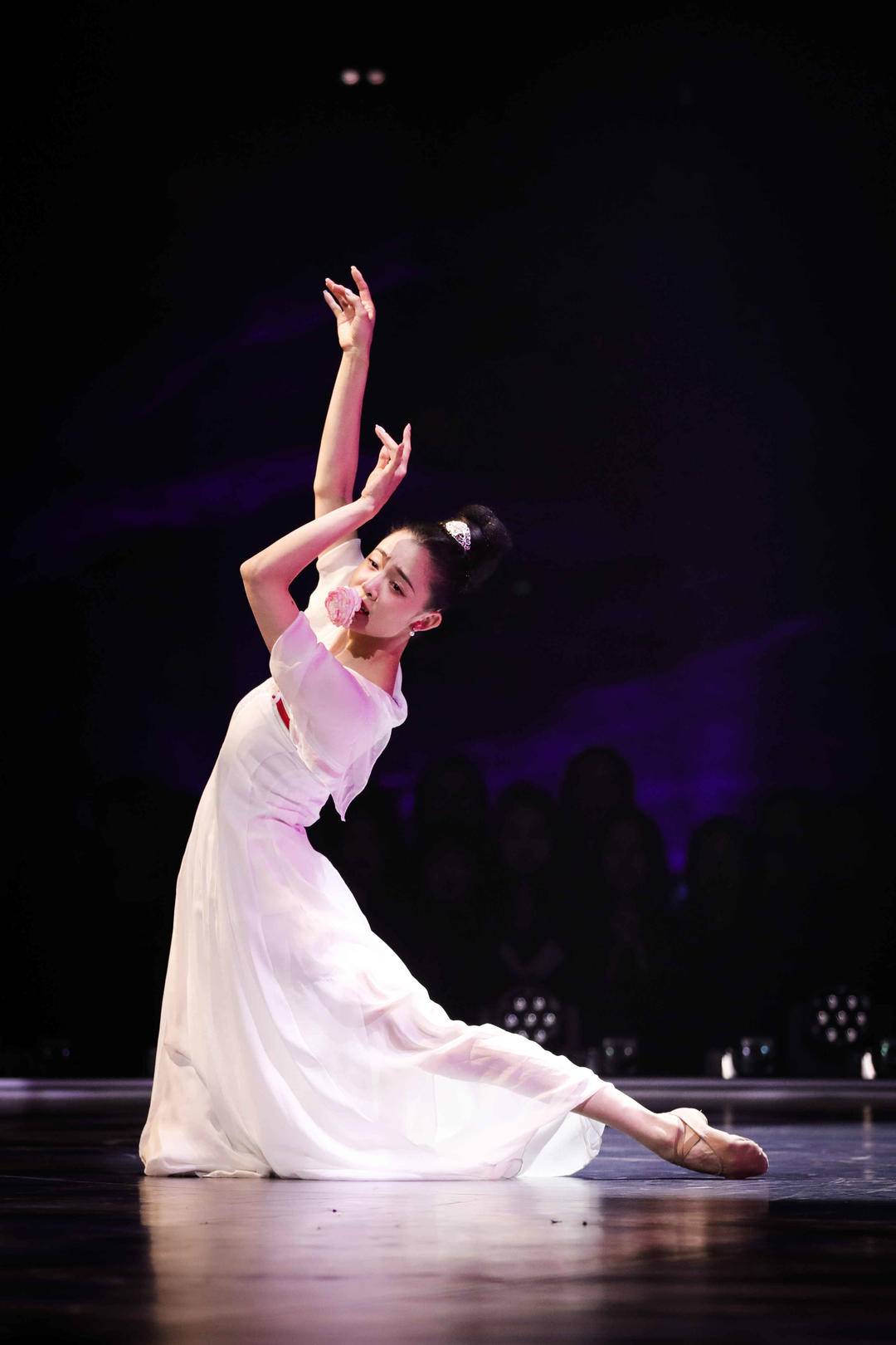 Dancer gracefully in a kneeling position with a flower in her mouth.