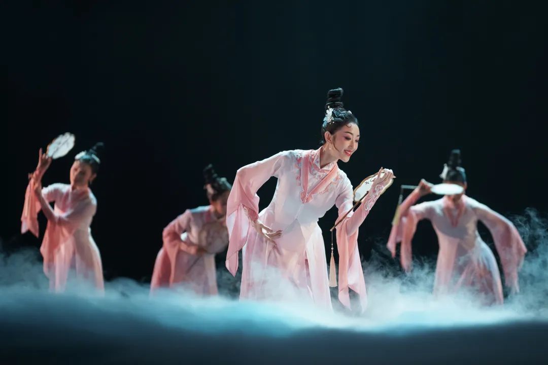 Group of dancers in a flowy pink costume with fans.