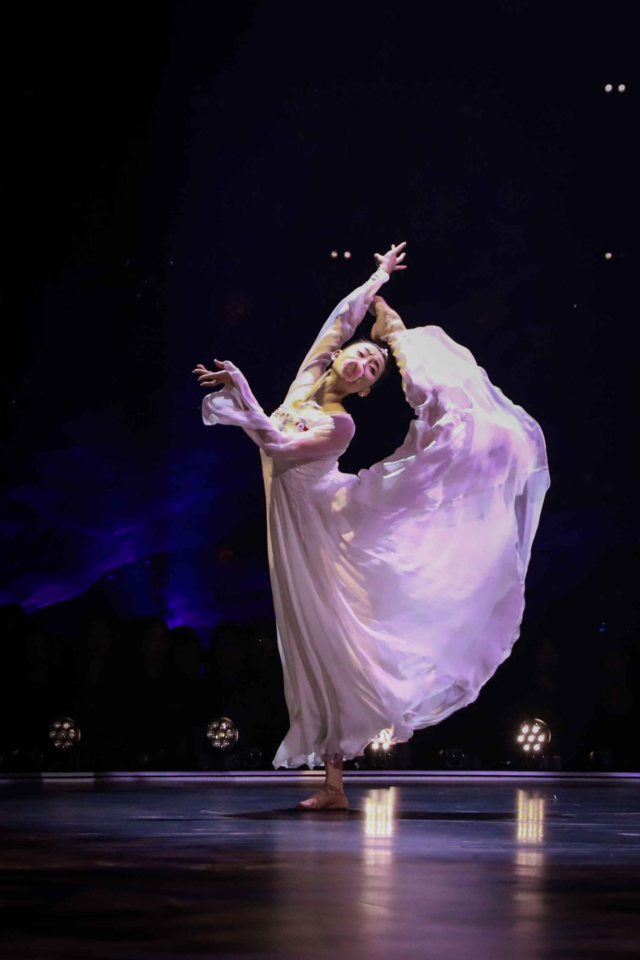Full body image of a dancer with a flower doing a leg kick.