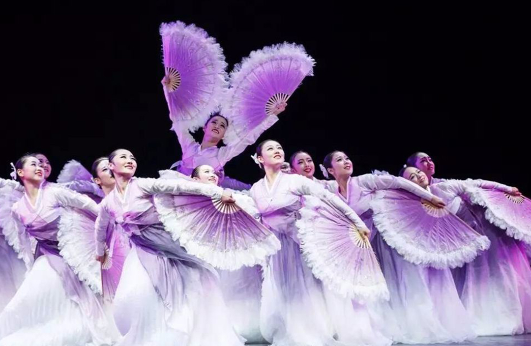 Dancers performing in a group with purple fans.