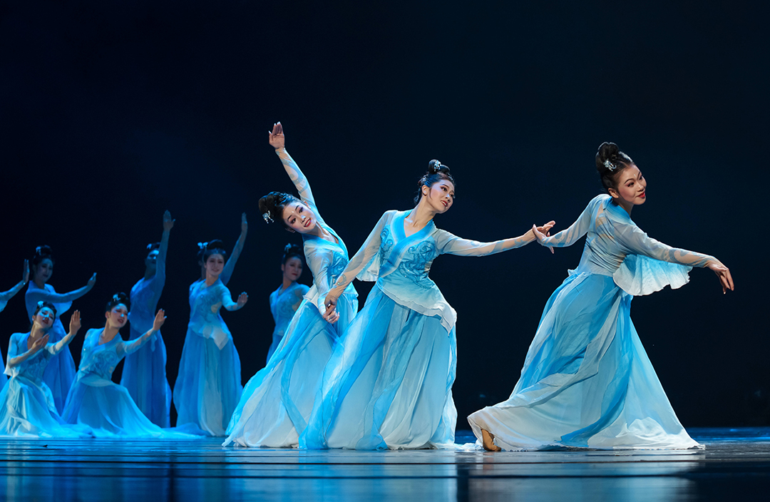 Group of dancers in blue on stage performing.