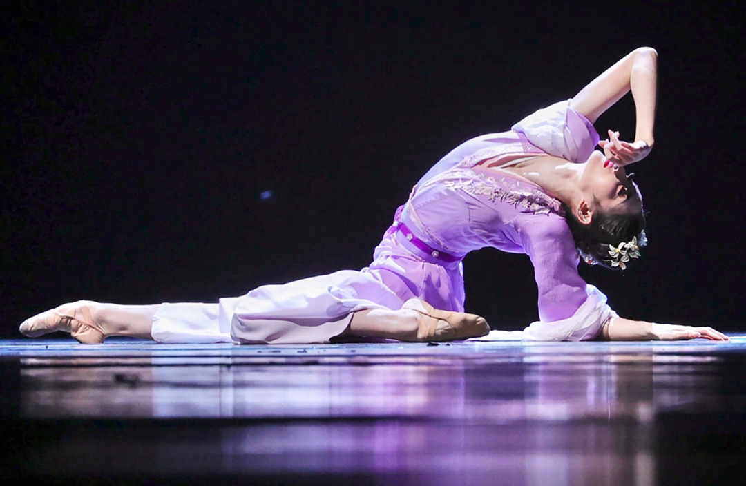 Dancer in purple sitting in a pose on stage.