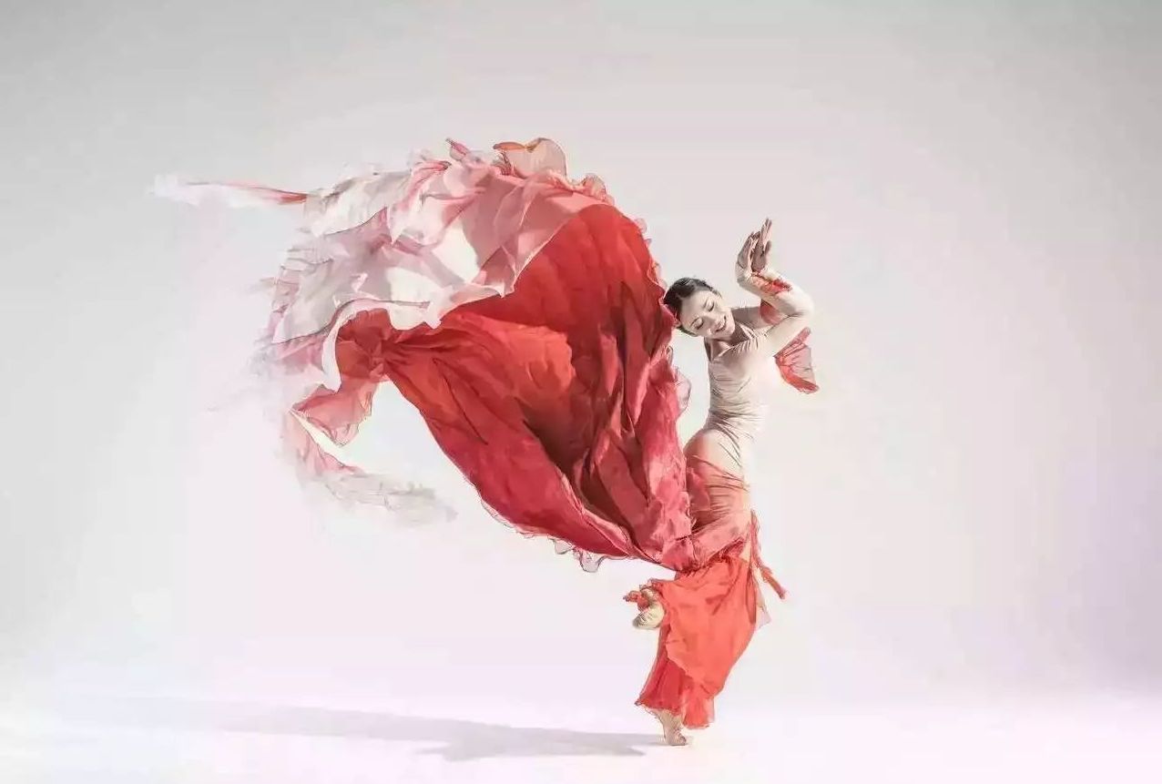 Dancer posing in a red costume kicking up her dress.